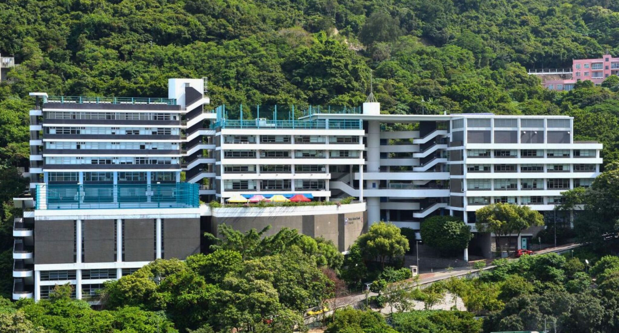 White multi-storey school buildings set into a steep wooded hillside